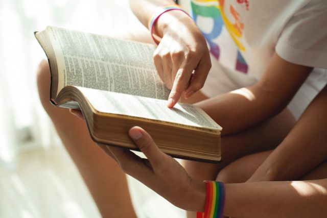 Bild mit Händen, die ein Buch halten, ein Finger zeigt auf die Buchseite 